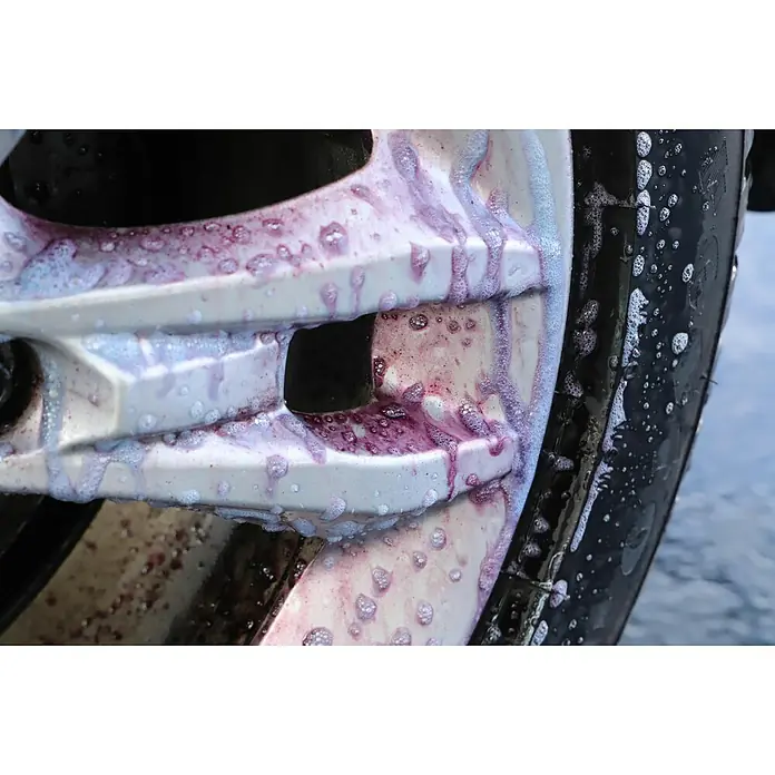 Nigrin Felgenreiniger - Nettovolumen: 750 ml - Nahaufnahme einer silbernen Autofelge, die mit einem violetten Reiniger bedeckt ist, der Schmutz löst.\n