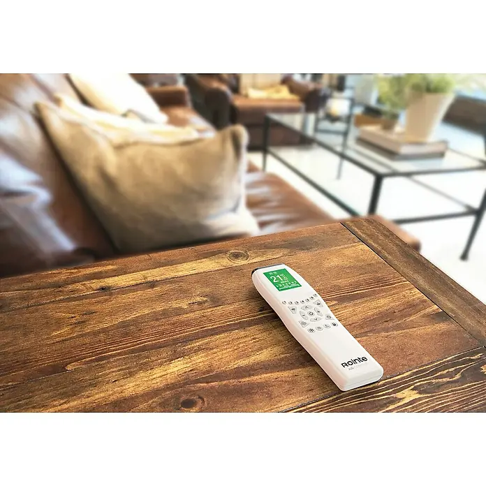 Rointe Mando a distancia AIR Control - Blanco - Primer plano de un mando a distancia de aire acondicionado Rointe sobre una mesa de madera, que permite ajustar fácilmente la temperatura en la habitación.