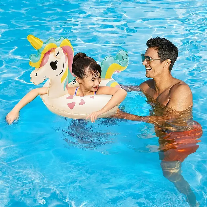 Funsicle Schwimmtier Einhorn - L x B x H: 76 x 53 x 55 cm - Ein Mädchen schwimmt mit einem aufblasbaren Einhorn im Pool, während ein Mann lächelnd daneben steht.