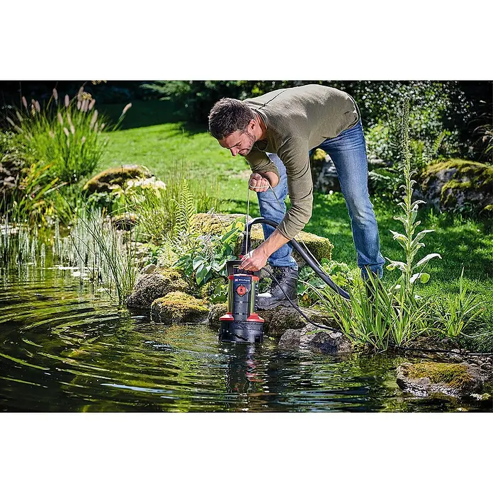 Einhell Schmutzwasserpumpe ECO GE-DP 7935 N-A - Max. Fördermenge: 19.500 l/h - Ein Mann bedient eine Einhell-Tauchpumpe zum Entleeren eines Gartenteichs, umgeben von üppiger Vegetation.