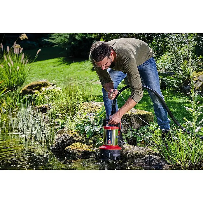 Einhell Schmutzwasserpumpe ECO GE-DP 7535 N LL - Max. Fördermenge: 18.500 l/h - Mann beugt sich über eine Einhell-Schmutzwasserpumpe am Rande eines Gartenteichs, um ihn zu entwässern.