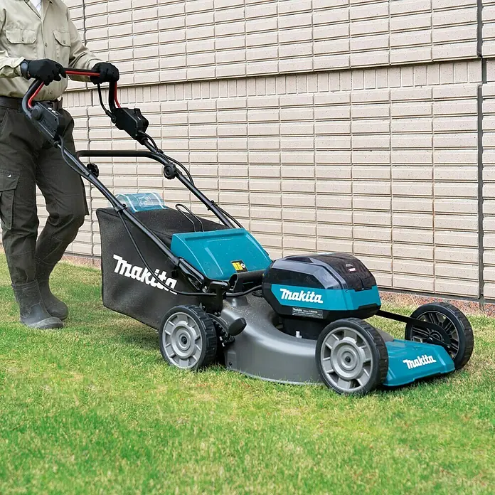 Makita XGT 40V max. Akku-Rasenmäher LM001GT204 - 40 V, 2 Akkus, 5 Ah, Schnittbreite: 48 cm - Eine Person schiebt einen Makita-Akku-Rasenmäher auf einer Grünfläche vor einer Hauswand.