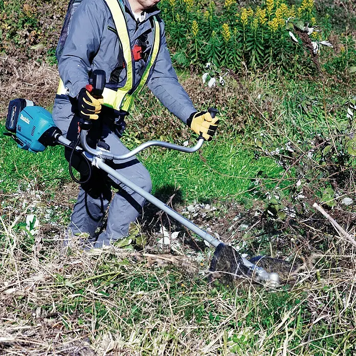 Makita XGT 40V max. Akku-Freischneider DUR013GZ04 - 40 V, Ohne Akku, Schnittbreite Messer: 255 mm - Eine Person benutzt einen Makita Akku-Rasentrimmer mit gelben Handschuhen, um Gras zu schneiden.