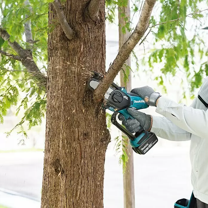 Makita LXT 18V Akku-Astsäge DUC101RF01 - 18 V, 3 Ah, 1 Akku - Person nutzt türkisfarbene Makita Akku-Minikettensäge zum Schneiden eines Astes, Sägespäne fliegen.