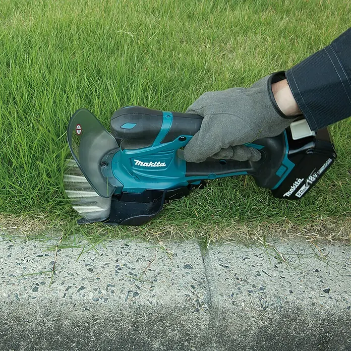 Makita LXT 18V Akku-Gras- & Strauchschere DUM604RFX1 - 18 V, Li-Ionen, 1 Akku - Eine Person benutzt einen Makita Akku-Kantenschneider, um Rasenkanten zu trimmen. Das Werkzeug ist kompakt und benutzerfreundlich.