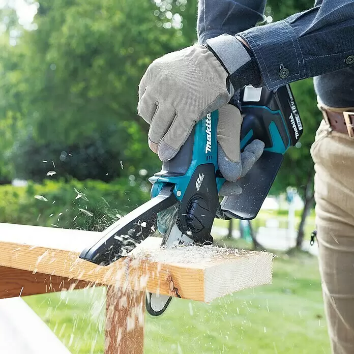 Makita LXT 18V Akku-Astsäge DUC101RF01 - 18 V, 3 Ah, 1 Akku - Eine Person in grauen Handschuhen schneidet mit einer türkis-schwarzen Makita Mini-Kettensäge ein Holzbrett, wobei Sägespäne fliegen.