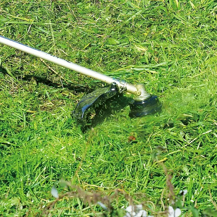 Makita Fadenkopf TAP&GO 1911Y2-9 - Passend für: Makita Akku-Freischneider UR013G - Ein Rasentrimmer schneidet hohes Gras, wobei der Schutzschild gut sichtbar ist. Das Gerät ist im Einsatz und sorgt für einen gepflegten Garten.