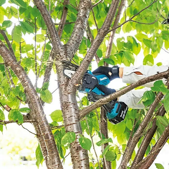 Makita LXT 18V Akku-Astsäge DUC101RF01 - 18 V, 3 Ah, 1 Akku - Eine blaue und schwarze Makita Kettensäge schneidet einen Ast, bedient von einer behandschuhten Hand. Späne fliegen beim Beschneiden.
