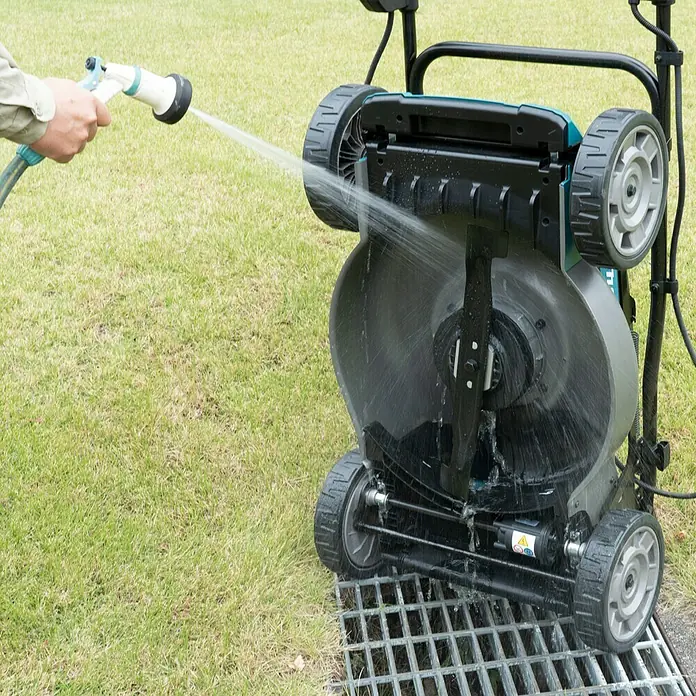 Makita XGT 40V max. Akku-Rasenmäher LM001GT204 - 40 V, 2 Akkus, 5 Ah, Schnittbreite: 48 cm - Eine Rasenmäher-Unterseite wird mit einem Schlauch gereinigt, um Grasreste zu entfernen. Hilft die Lebensdauer des Geräts zu verlängern.