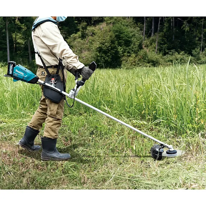Makita XGT 40V max. Akku-Motorsense UR016GZ - 40 V, Ohne Akku, Schnittbreite Messer: 230 mm - Ein Mann mäht Gras mit einem Makita Akku-Rasentrimmer in einem grünen Feld, umgeben von Bäumen.
