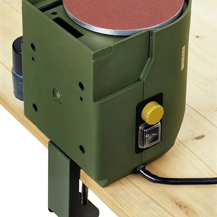 Proxxon Tellerschleifgerät TG 125/E - 140 W, 125 mm, 800 m/min - Nahaufnahme einer Proxxon Tischbandschleifmaschine mit Schleifscheibe, montiert auf einer Holzwerkbank, mit gut sichtbarem Schalter.