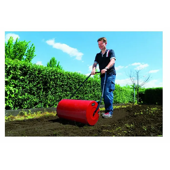 Einhell Rodillo para césped GC-GR 57 - Anchura de trabajo: 57 cm, Diámetro: 32 cm - Un hombre usa un rodillo de jardín para aplanar el suelo. El rodillo rojo y el jardín verde al fondo crean un contraste agradable.