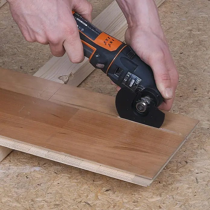 Wolfcraft Sägeblatt für Vibrationssäge halbrund - 85 mm, HS-Stahl - Das Bild zeigt eine Nahaufnahme eines Mannes, der mit einem oszillierenden Multifunktionswerkzeug ein Stück Holz schneidet.