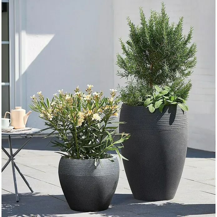 Scheurich Lineo Pflanzsäule rund - Außenmaß (Ø x H): 47 x 65 cm, Kunststoff, Schwarz - Zwei dekorative Pflanzgefäße in verschiedenen Größen mit üppigen Pflanzen auf einer Terrasse.