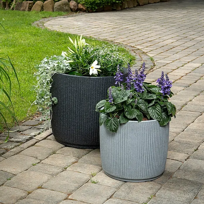 Scheurich Pflanzkübel rund Linetto - Außenmaß (Ø x H): 38,6 x 35,2 cm, Kunststoff, Stony Black - Zwei stilvolle Pflanzgefäße in Grau und Anthrazit mit bunten Blumenarrangements auf einem gepflasterten Weg.