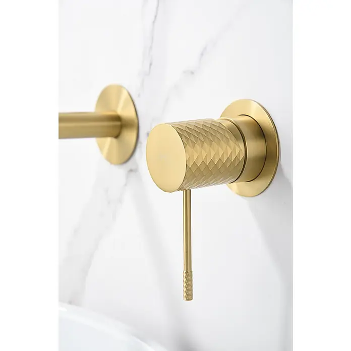 Imex Génova Grifo de lavabo empotrado - Oro - Grifo dorado de lavabo montado en la pared con un mango texturizado y diseño minimalista sobre fondo de mármol blanco.