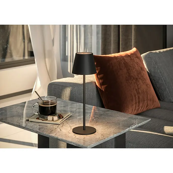Starlux Paola Akku-Tischleuchte - 3 W, L x B x H: 11 x 11 x 36 cm, Schwarz, Warmweiß - Elegante kabellose Lampe in Schwarz auf einem Marmortisch neben einer Tasse Kaffee und einem Sofa. Perfekt für gemütliche Abende.