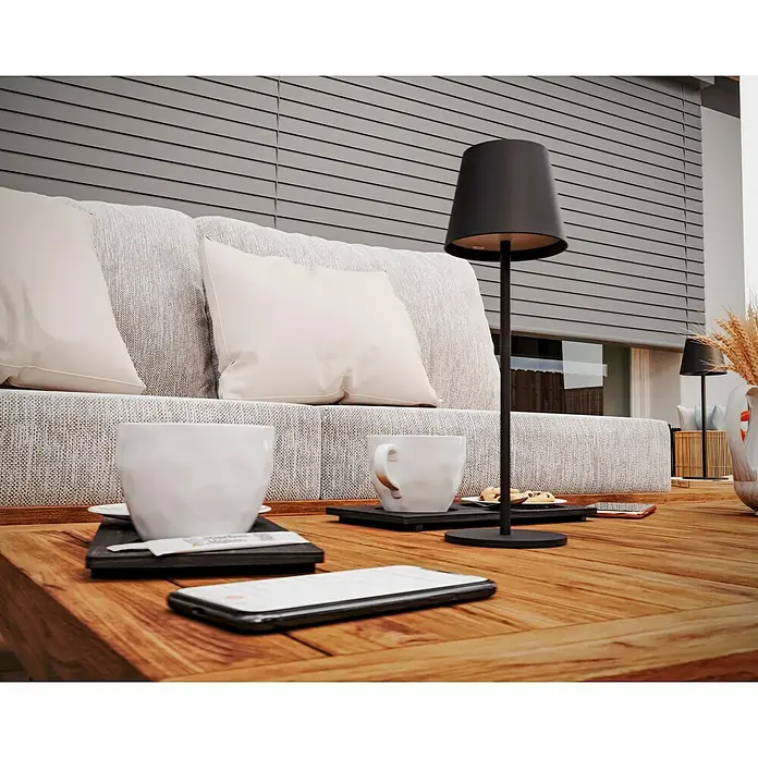 Starlux Paola Akku-Tischleuchte - 3 W, L x B x H: 11 x 11 x 36 cm, Schwarz, Warmweiß - Einladende Szene mit einer modernen schwarzen Tischlampe, stilvollen Tassen und Smartphones auf einem Holztisch, der zum Verweilen einlädt.