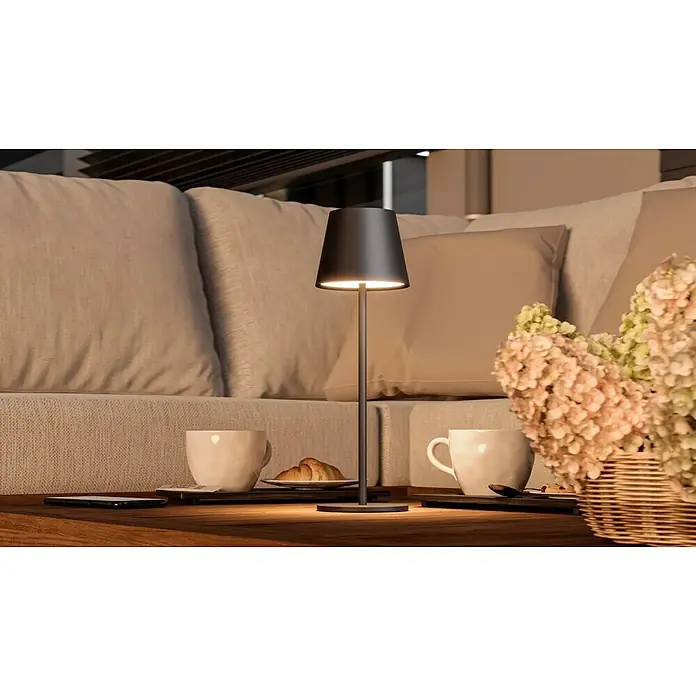 Starlux Paola Akku-Tischleuchte - 3 W, L x B x H: 11 x 11 x 36 cm, Schwarz, Warmweiß - Ein stimmungsvolles Bild zeigt eine moderne Tischleuchte auf einem Couchtisch mit Getränken und Snacks.
