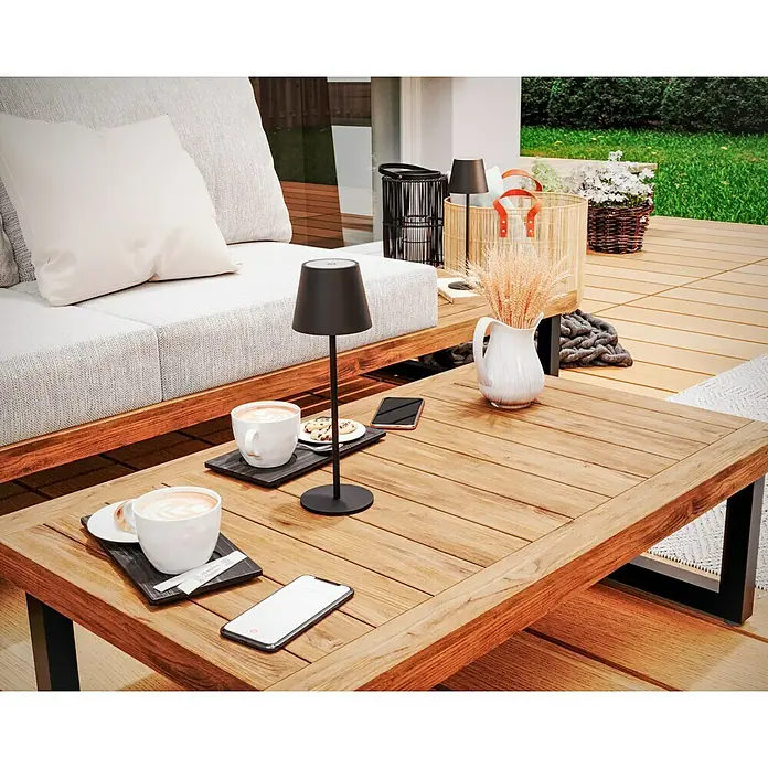 Starlux Paola Akku-Tischleuchte - 3 W, L x B x H: 11 x 11 x 36 cm, Schwarz, Warmweiß - Ein stilvoller Außenbereich mit einer modernen Lampe auf einem Holztisch, neben Kaffeetassen und Handys.