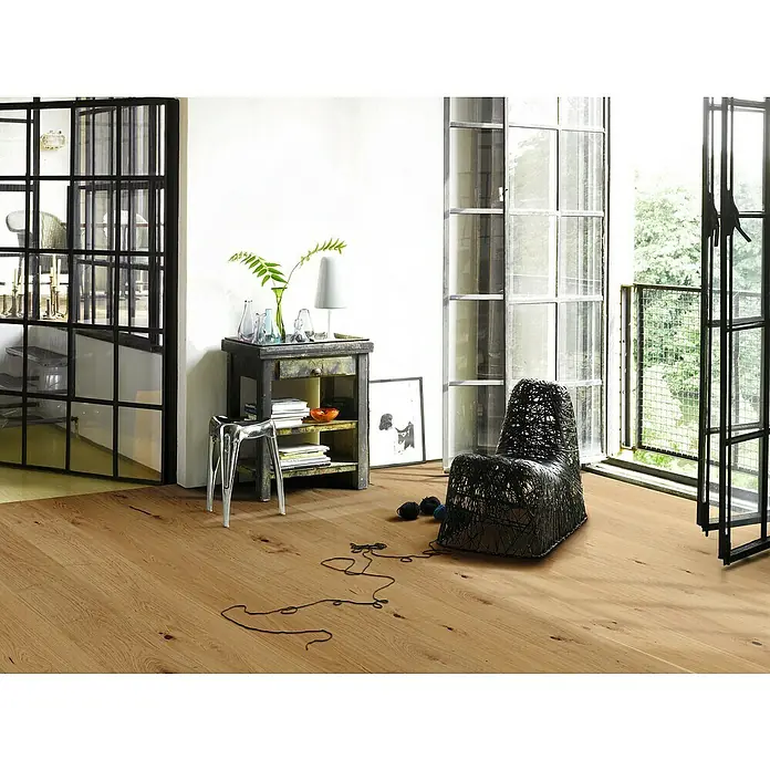 Parador Parkett Classic 3025 - Rustikal Eiche, Landhausdiele, 2.380 x 233 x 13 mm - Einrichtung mit hellbraunem Holzboden, einem schwarzen Sessel und großen Fenstern, die eine moderne, einladende Atmosphäre schaffen.