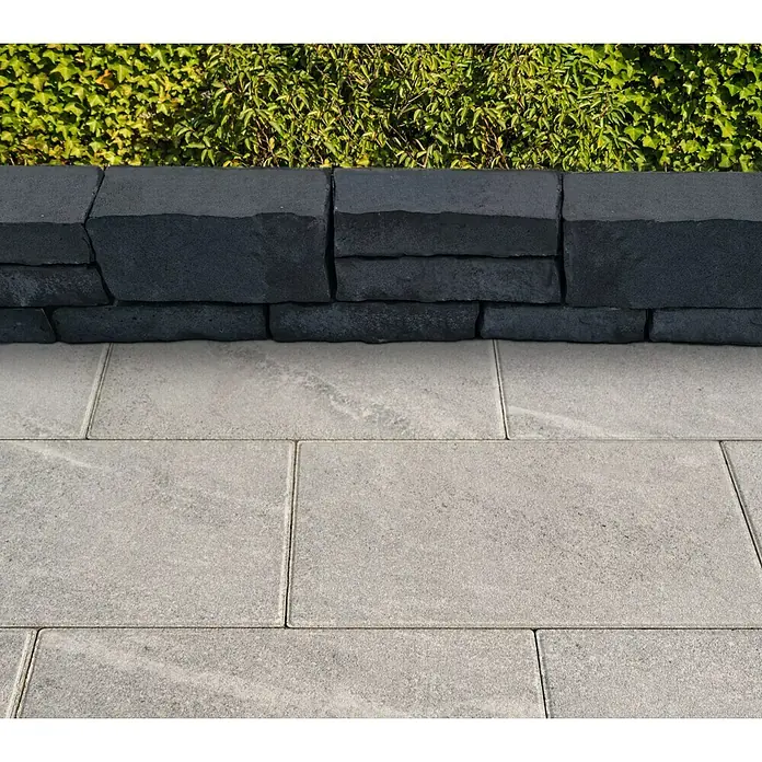 Diephaus Mauerstein Victorville - L x B x H: 40 x 20 x 10 cm, Basalt, Beton - Stilvolles Außenbereich-Design mit grauen Pflastersteinen und einer dunklen Steinmauer, ergänzt durch grünes Laub. Eine elegante Gartengestaltung.