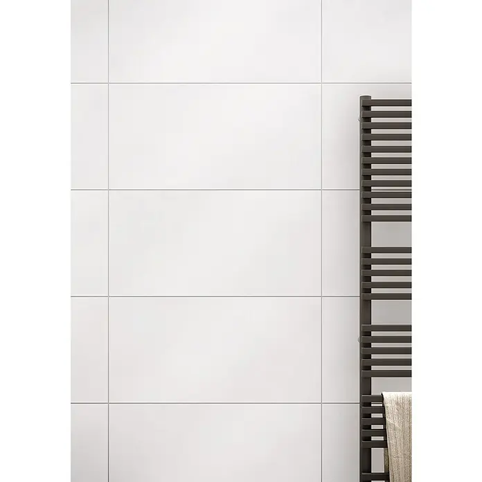 Wandfliese Zürich New - 30 x 60 cm, Weiß, Matt - Nahaufnahme einer weißen gefliesten Wand mit einem modernen, dunklen Handtuchwärmer, der Eleganz und Funktionalität vereint.