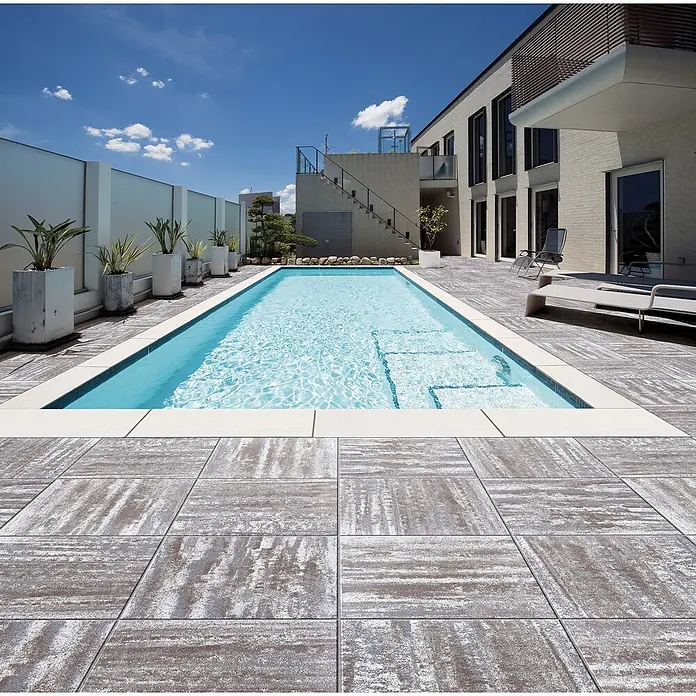 Terrassenplatte Megadrain Tundra - 50 x 50 x 4 cm, Hellgrau/Braun, Beton - Ein luxuriöser Außenpool mit grauen Fliesen umgeben, der einen modernen und stilvollen Raum zum Entspannen schafft. Die klaren Linien des Pools ergänzen das Gebäude.