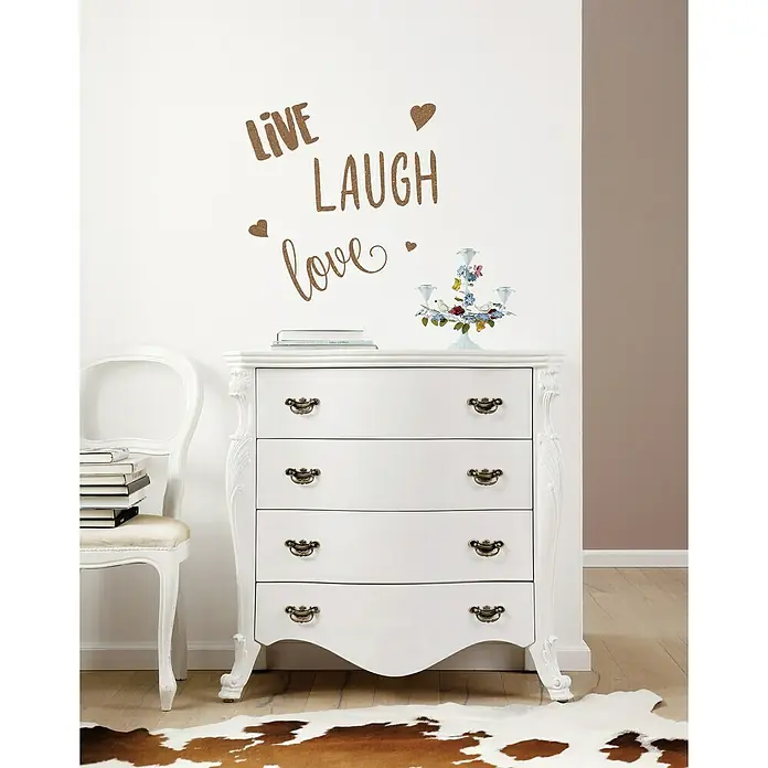 Komar Dekosticker Live Laugh Love - 6 -tlg., 70 x 50 cm - Eine weiße Kommode mit vier Schubladen und verschnörkelten Details. Auf der Kommode stehen ein Buch und ein Kerzenständer.
