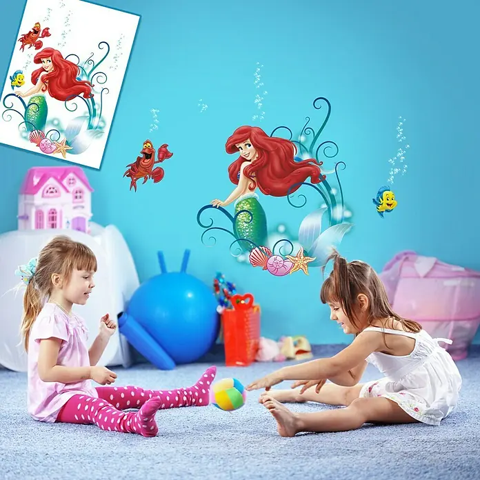 Komar Wandtattoo Arielle - 70 x 50 cm - Kinder spielen in einem Raum mit einer Wanddekoration mit Arielle, der Meerjungfrau, und ihren Freunden, die eine lustige, verspielte Atmosphäre schaffen.