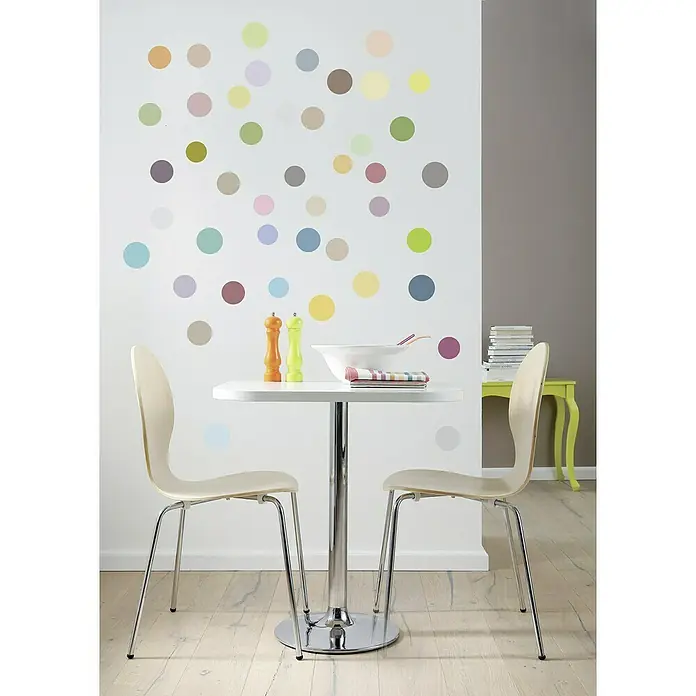 Komar Wandtattoo Dots - 70 x 50 cm - Ein minimalistischer Essbereich mit einem runden, weißen Tisch und zwei beigen Stühlen, dekoriert mit bunten Wandpunkten für eine spielerische Note.