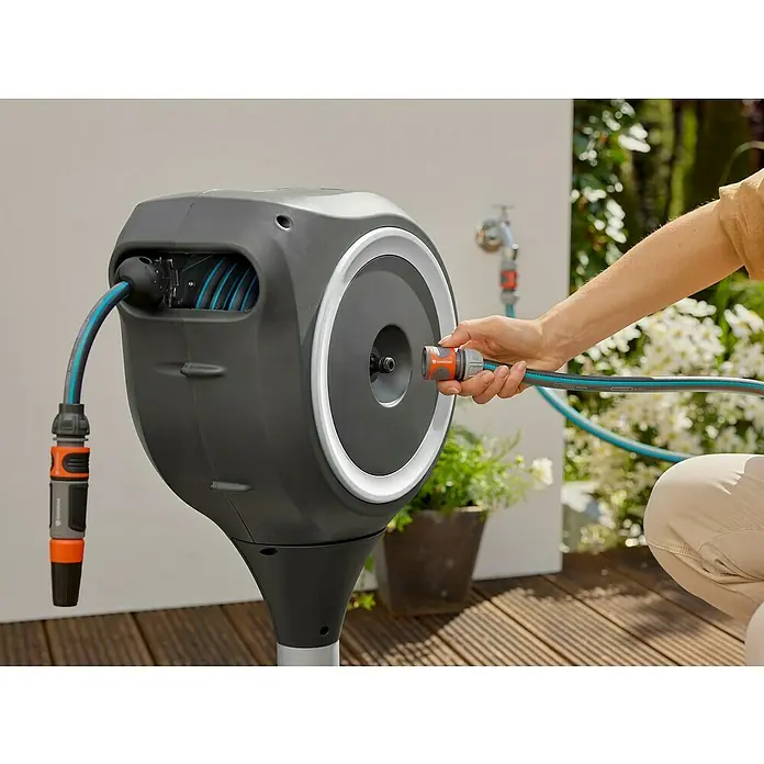 Gardena Schlauchbox Roll-Up S - Schlauchlänge: 15 m, 360 ° drehbar - Eine Gardena Schlauchbox an einem sonnigen Tag mit einer Person, die einen Schlauch anschließt.