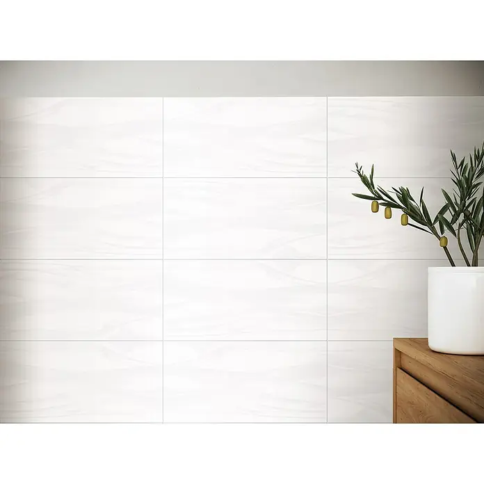 Wandfliese Macao New - 30 x 60 cm, Weiß, Matt - Nahaufnahme von glänzend weißen Fliesen, die an einer Wand angebracht sind, mit einem einfachen Holzschrank und einer Pflanze.