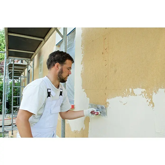 Steico Unterdeck- & Putzträgerplatte duo dry2.230 x 600 mm, Stärke: 60 mm, Wärmeleitfähigkeit: 0,043 W/(mK) - Ein Handwerker trägt mit einer Kelle Putz auf eine Fassade auf und glättet die Oberfläche, um sie zu verschönern.