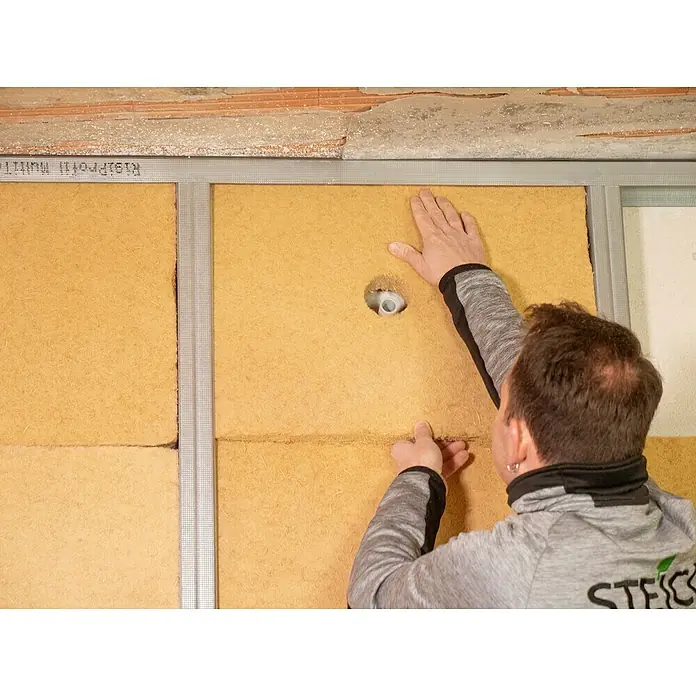 Steico Holzfaserdämmplatte flex 0381.200 x 625 mm, Stärke: 60 mm, Wärmeleitfähigkeit: 0,038 W/(mK), 7 Stk. - Wandmontage einer STEICO Holzfaserplatte zur Dämmung. Der Handwerker fixiert die Platte passgenau in einem Metallrahmen an der Wand.