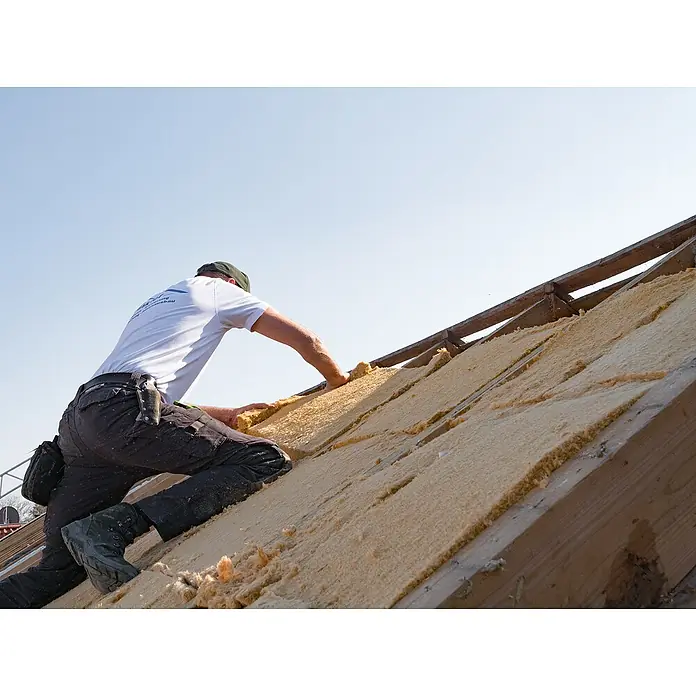 Steico Holzfaserdämmplatte flex 036 - 1.220 x 575 mm, Stärke: 40 mm, Wärmeleitfähigkeit: 0,036 W/(mK), 11 Stk. - Ein Dachdecker bei der Arbeit, der Isolierung auf einem Dach verlegt. Die Dämmstoffe sind hellbeige und passen sich der Dachstruktur an.