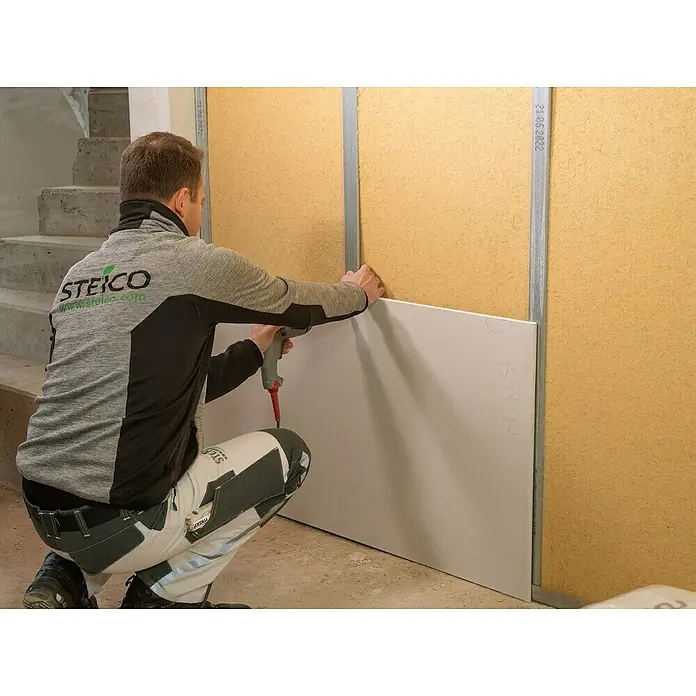 Steico Holzfaserdämmplatte flex 038 - 1.200 x 625 mm, Stärke: 60 mm, Wärmeleitfähigkeit: 0,038 W/(mK), 7 Stk. - Ein Handwerker befestigt eine STEICO Holzfaserplatte an einer Wandkonstruktion mit Metallprofilen. STEICO steht für ökologische Bauprodukte.