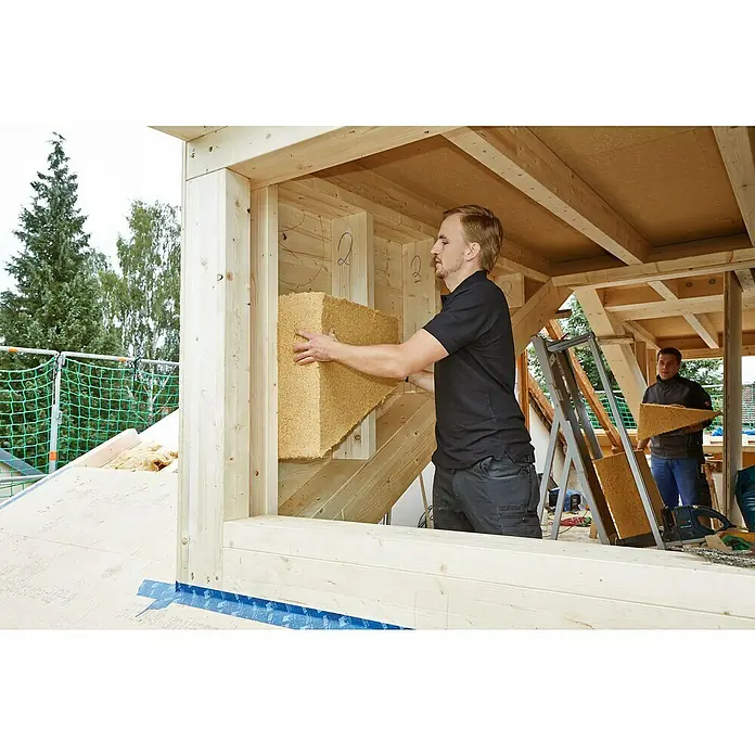 Steico Holzfaserdämmplatte flex 0361.220 x 575 mm, Stärke: 30 mm, Wärmeleitfähigkeit: 0,036 W/(mK), 14 Stk. - Ein Mann montiert eine Holzfaserdämmplatte in einem Holzrahmenbau, während ein anderer Mann im Hintergrund eine weitere Platte hält.