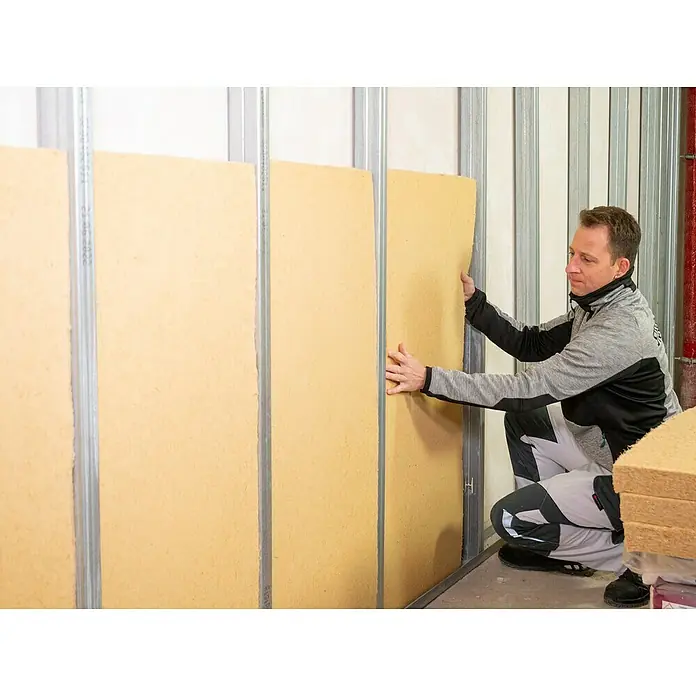 Steico Holzfaserdämmplatte flex 0381.200 x 625 mm, Stärke: 60 mm, Wärmeleitfähigkeit: 0,038 W/(mK), 7 Stk. - Ein Mann bringt Dämmplatten aus Holzfaser an einer Metallständerwand an.  Die Platten sind hellbraun und haben eine unebene Oberfläche.