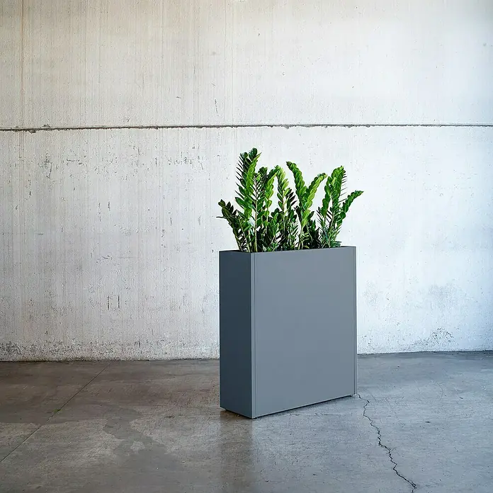 Herstera Garden Pflanzkasten Cube - L x B x H: 100 x 40 x 115 cm - Ein schlanker, grauer Pflanzkasten mit üppigem Grün steht vor einer schlichten Betonwand und bringt modernes Flair in den Raum.