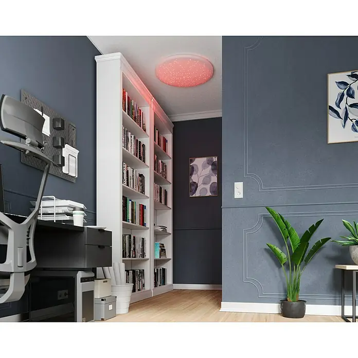 Tween Light LED-Deckenleuchte rund Skyler Star RGBW - 80 W, Ø x H: 74 x 10 cm, Weiß, RGBW - Ein moderner Raum mit einem Bücherregal und einer hellen, runden Deckenleuchte, die ein warmes, rotes Licht ausstrahlt. Schreibtisch & Dekoration vervollständigen den Raum.