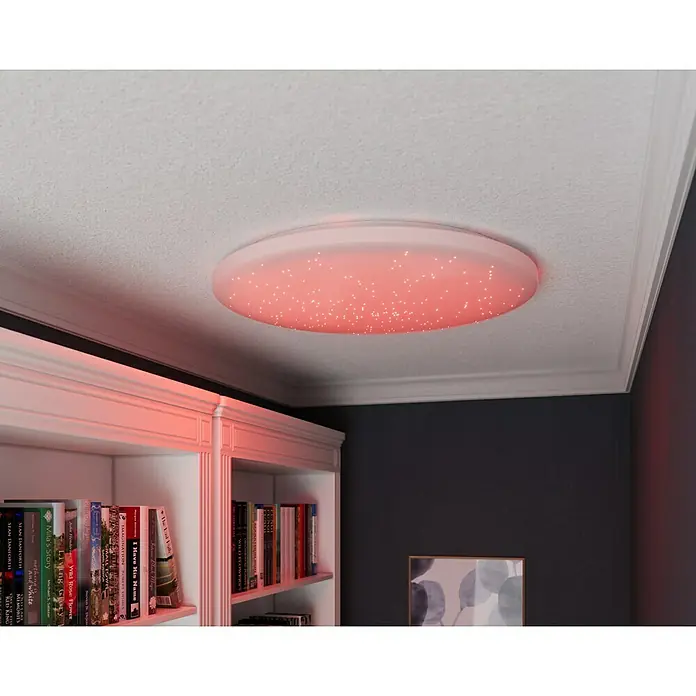 Tween Light LED-Deckenleuchte rund Skyler Star RGBW - 80 W, Ø x H: 74 x 10 cm, Weiß, RGBW - Eine moderne, runde LED-Deckenleuchte mit Sterneneffekt in einem Raum mit Bücherregal.