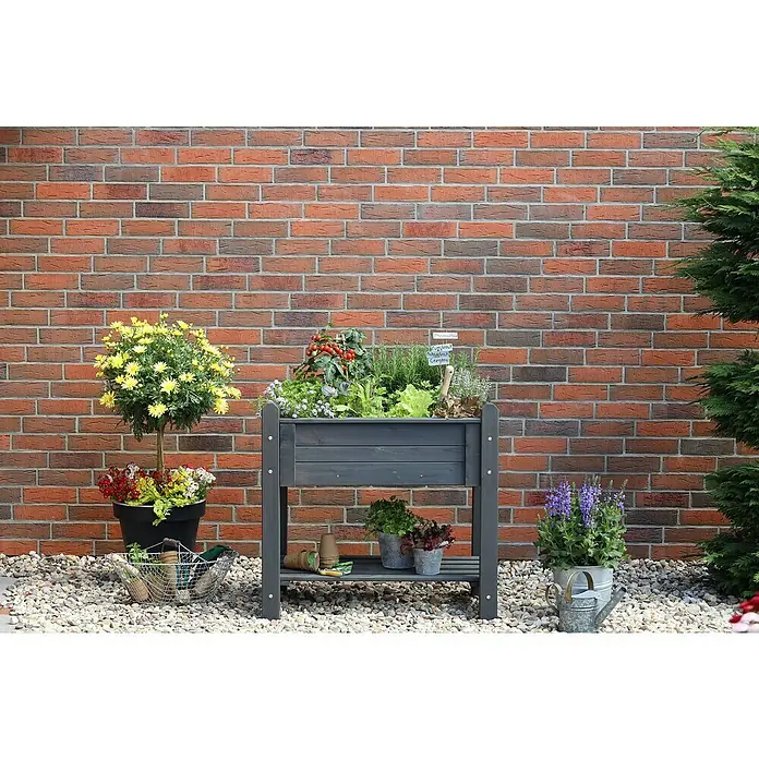 Promadino Kräuterhochbeet - 90 x 60 x 84,5 cm, Grau - Das Bild zeigt einen grauen, erhöhten Gartenkasten mit verschiedenen Pflanzen, der vor einer roten Backsteinmauer steht.