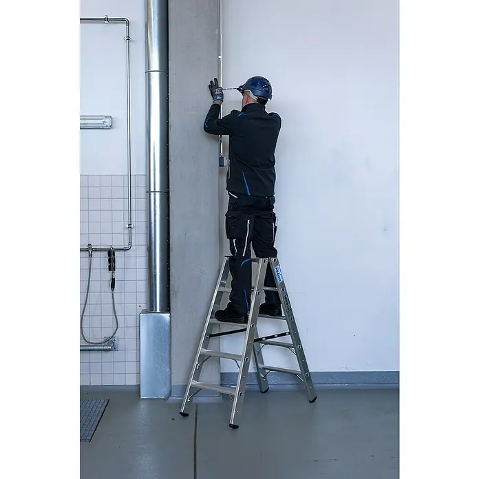 Krause Stabilo Doppel-Stehleiter 2 x 5 Stufen - Anzahl Tritte: 10 Stk., Arbeitshöhe: 2,7 m, Belastbarkeit: 225 kg, Aluminium - Ein Handwerker auf einer Krause Leiter befestigt eine Leitung an der Wand. Die Leiter ist aus Aluminium und hat mehrere Stufen.