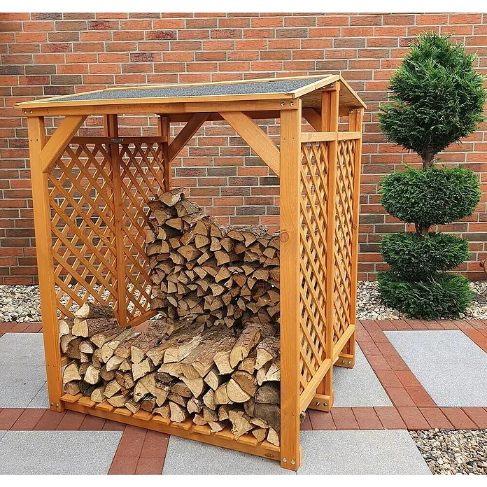 Promadino Kaminholzregal - 120 x 118 x 148 cm, Holz, Braun - Holzlager mit Lattenrost-Seitenwänden und geneigtem Dach, gefüllt mit Holzscheiten, vor einer Ziegelmauer und einem Zierbaum.