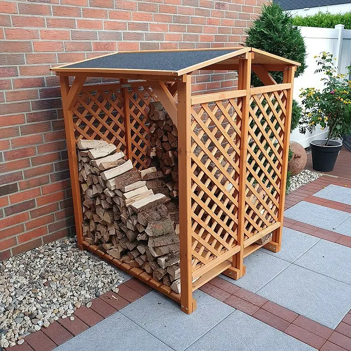 Promadino Kaminholzregal - 120 x 118 x 148 cm, Holz, Braun - Ein hölzerner Kaminholzunterstand mit Gitterstruktur, gefüllt mit Holzscheiten, steht an einer Backsteinmauer auf einem gepflasterten Untergrund.