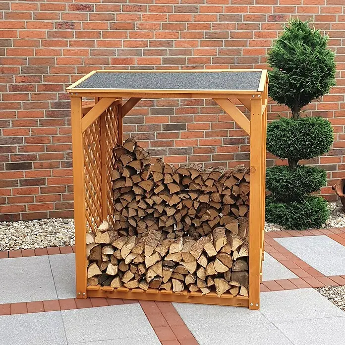 Promadino Kaminholzregal - 120 x 118 x 148 cm, Holz, Braun - Brennholzregal aus Holz mit Dach, gefüllt mit Holzscheiten, vor einer Backsteinmauer und einem grünen Busch.
