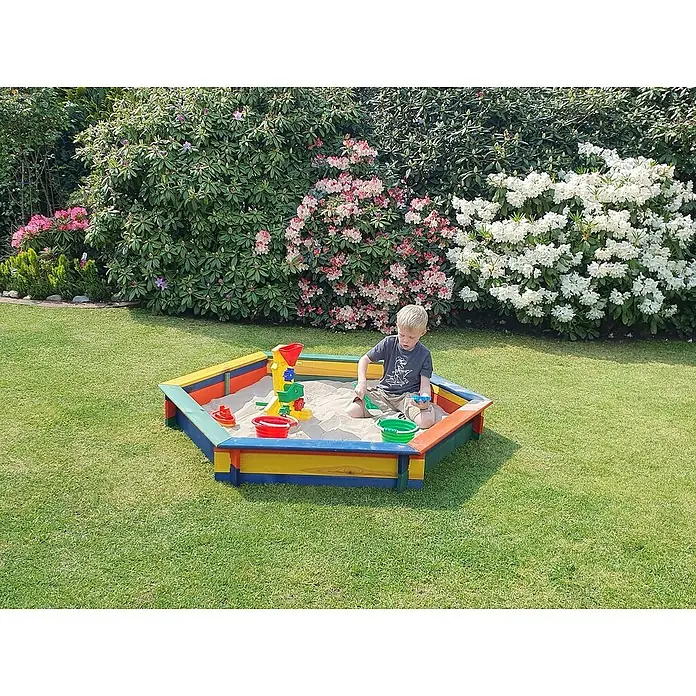 Promadino 6-Eck-Sandkasten Fynja - 173 x 148 x 21 cm, Kiefer, Bunt - Ein Junge spielt in einem farbenfrohen Sandkasten im Garten, umgeben von blühenden Büschen und grünem Rasen.