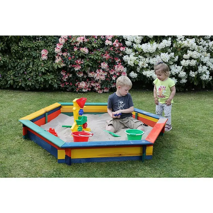 Promadino 6-Eck-Sandkasten Fynja - 173 x 148 x 21 cm, Kiefer, Bunt - Ein farbenfroher Sandkasten mit einem Jungen darin, daneben ein kleines Mädchen, umgeben von blühenden Büschen im Garten.