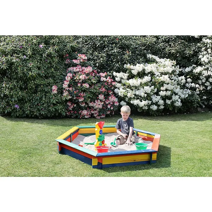 Promadino 6-Eck-Sandkasten Fynja - 173 x 148 x 21 cm, Kiefer, Bunt - Ein Junge spielt in einem farbenfrohen Sandkasten mit Sandspielzeug, umgeben von üppigem Grün und blühenden Büschen.